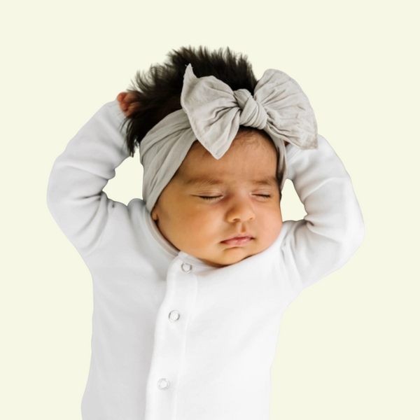 Sleeping baby wearing a neutral Baby Bling nylon knot headband and white sleeper