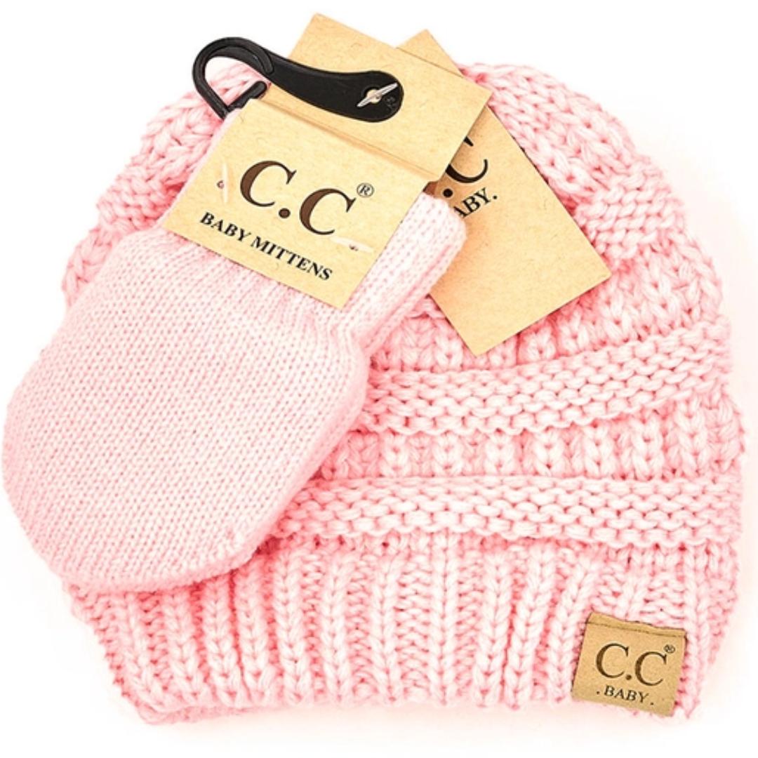 Pink knitted baby hat and mittens set with C.C Baby tags on a white background