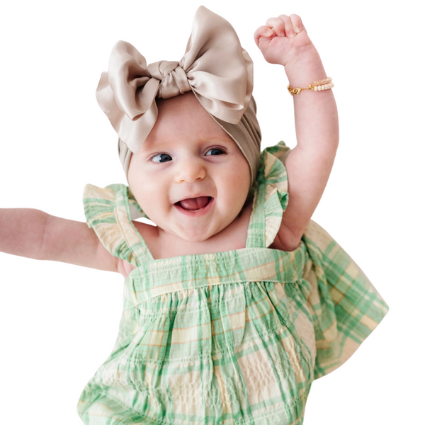 Baby wearing a champagne satin knot headband with a green plaid outfit 