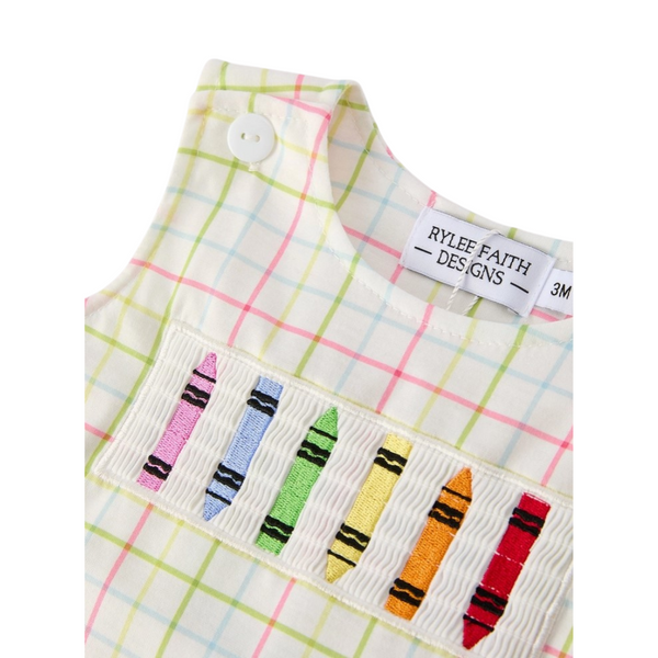 Close-up of embroidered crayons on a smocked panel of a pastel plaid romper with white button at the shoulder.
