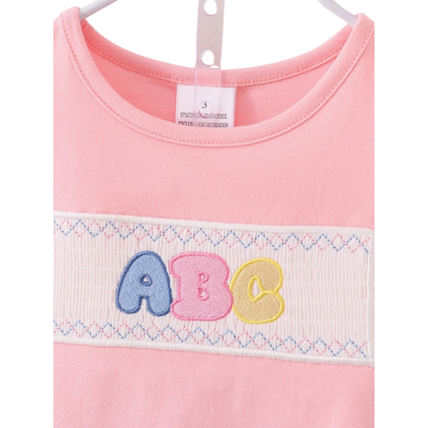 Close-up of ABC embroidery on the smocked chest of the pink girls' top, with pastel stitching.