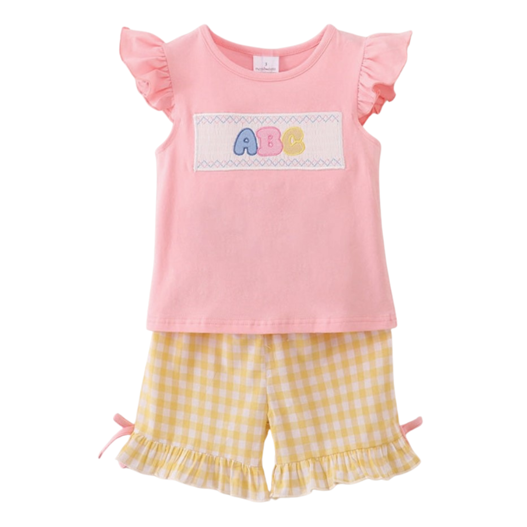 Front view of pink flutter sleeve top with ABC smocking and yellow gingham ruffle shorts for girls.