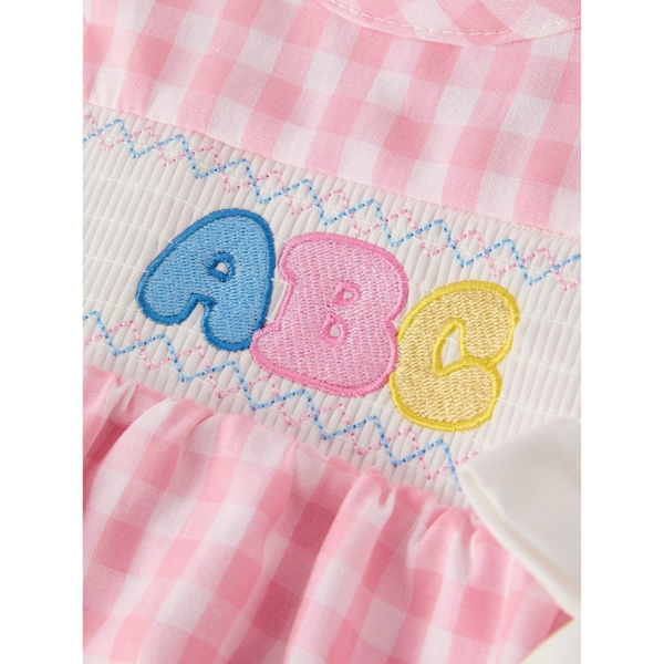 Close-up of the ABC applique detail on a smocked white panel, featuring blue, pink, and yellow letters with zigzag embroidery.