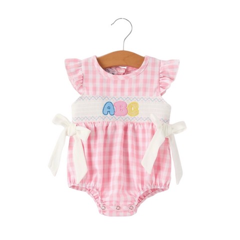 Front view of a baby girl’s pink gingham romper with ruffle sleeves, white side bows, and colorful ABC applique on a smocked chest.