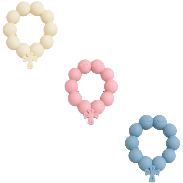 Nola Tawk Blessing Beads ring teethers with cross pendants shown in soft ivory, pink and blue on a white background.