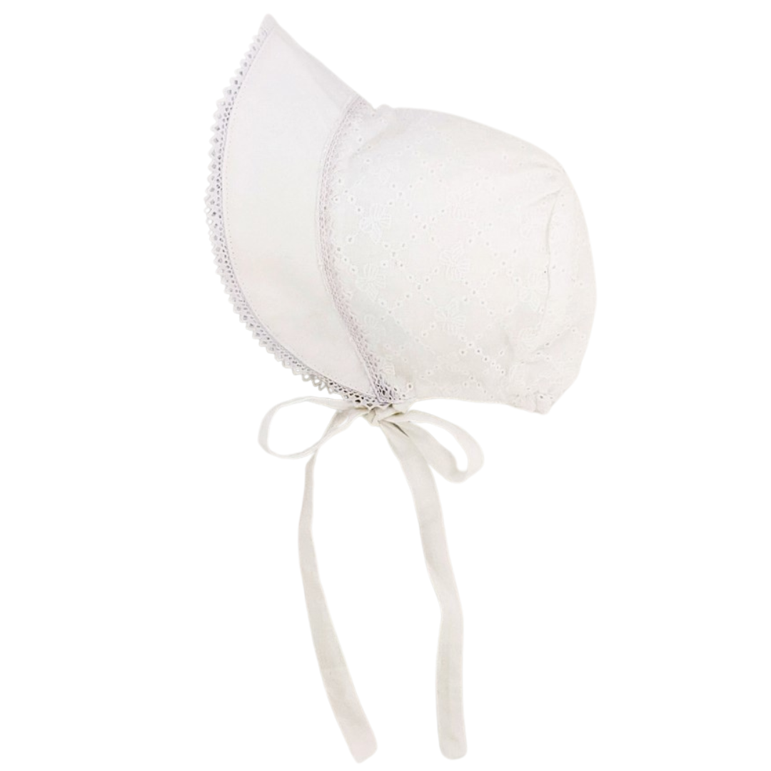 White baby bonnet with bow eyelet embroidery, scalloped brim trim, and chin ties, displayed on flat surface.