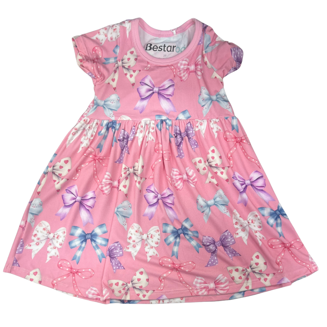Pink short-sleeve dress with colorful all-over bow print in various patterns, featuring a gathered waist and full skirt.