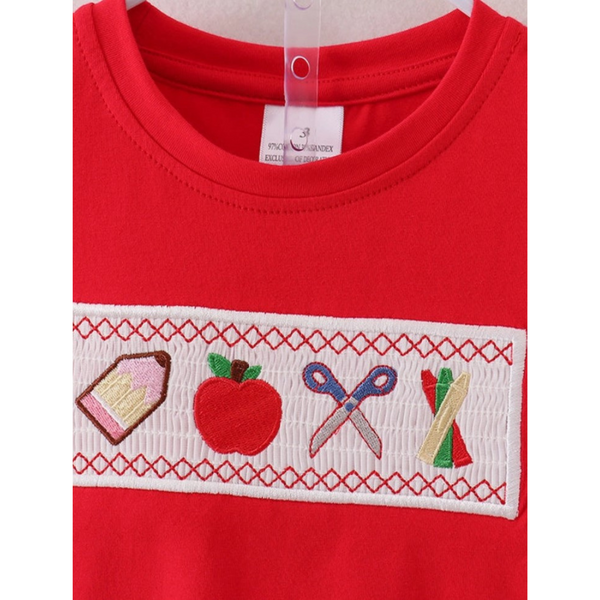 Close-up of red tee with smocked embroidery showing a pencil, apple, scissors, and crayons on a back-to-school boys’ outfit.