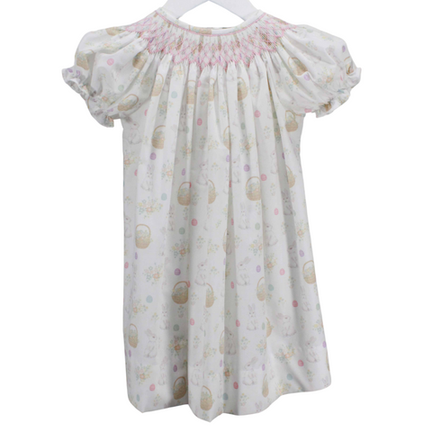 Hand-smocked  short sleeve bishop dress featuring delicate geometric smocking in pink on a soft, watercolor print of bunnies and Easter baskets. A sweet and feminine design.