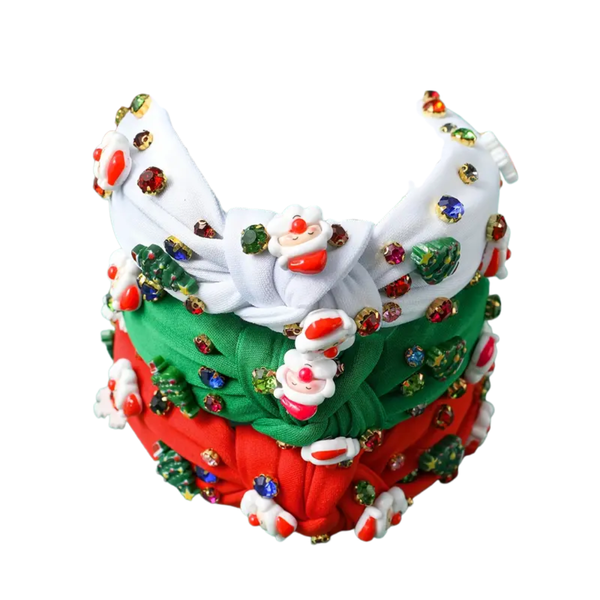A stack of three festive knotted headbands in white, green, and red, each heavily embellished with colorful rhinestones, small Christmas trees, and cute Santa Claus charms.