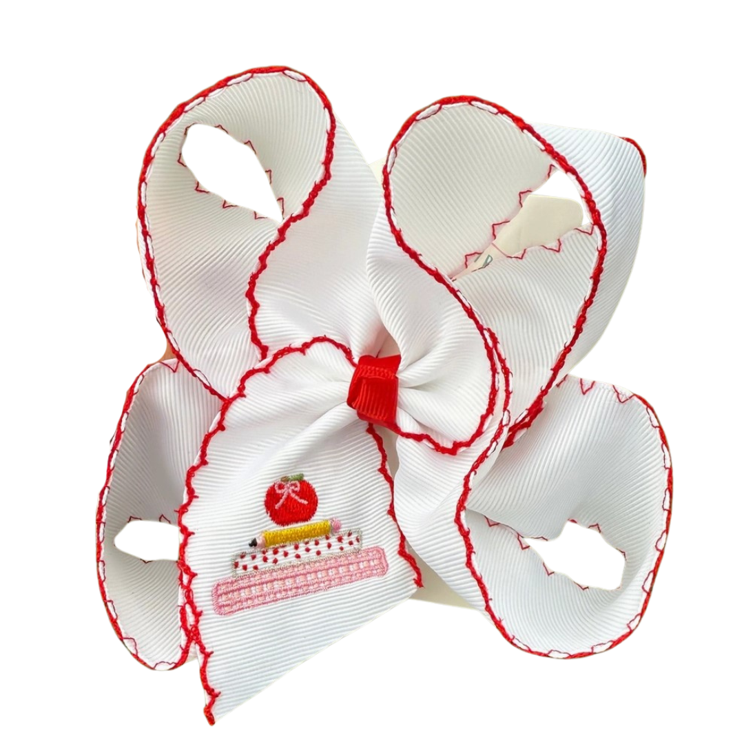 White grosgrain hair bow with red scalloped edges and embroidery of stacked books topped with a red apple on the bow tail.