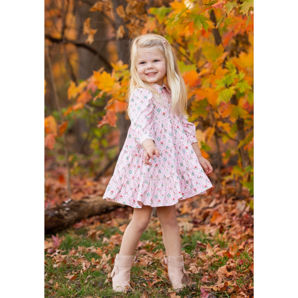Young girl wearing the Dixie Dress in a fall setting with colorful leaves, smiling and pointing while posing in pink boots.