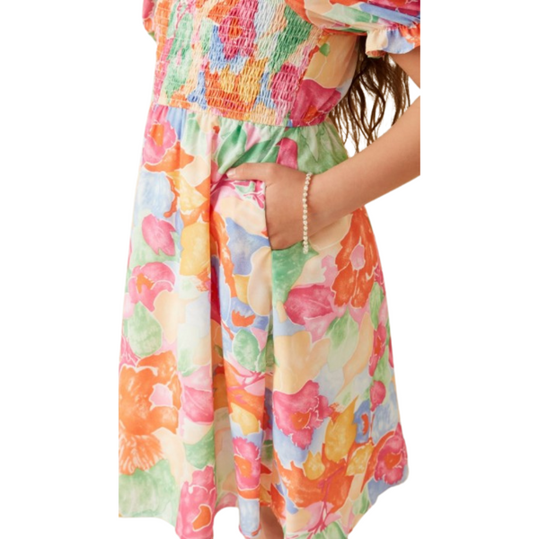 Close-up of the dress highlighting smocked bodice, side pocket, and vibrant watercolor floral fabric.
