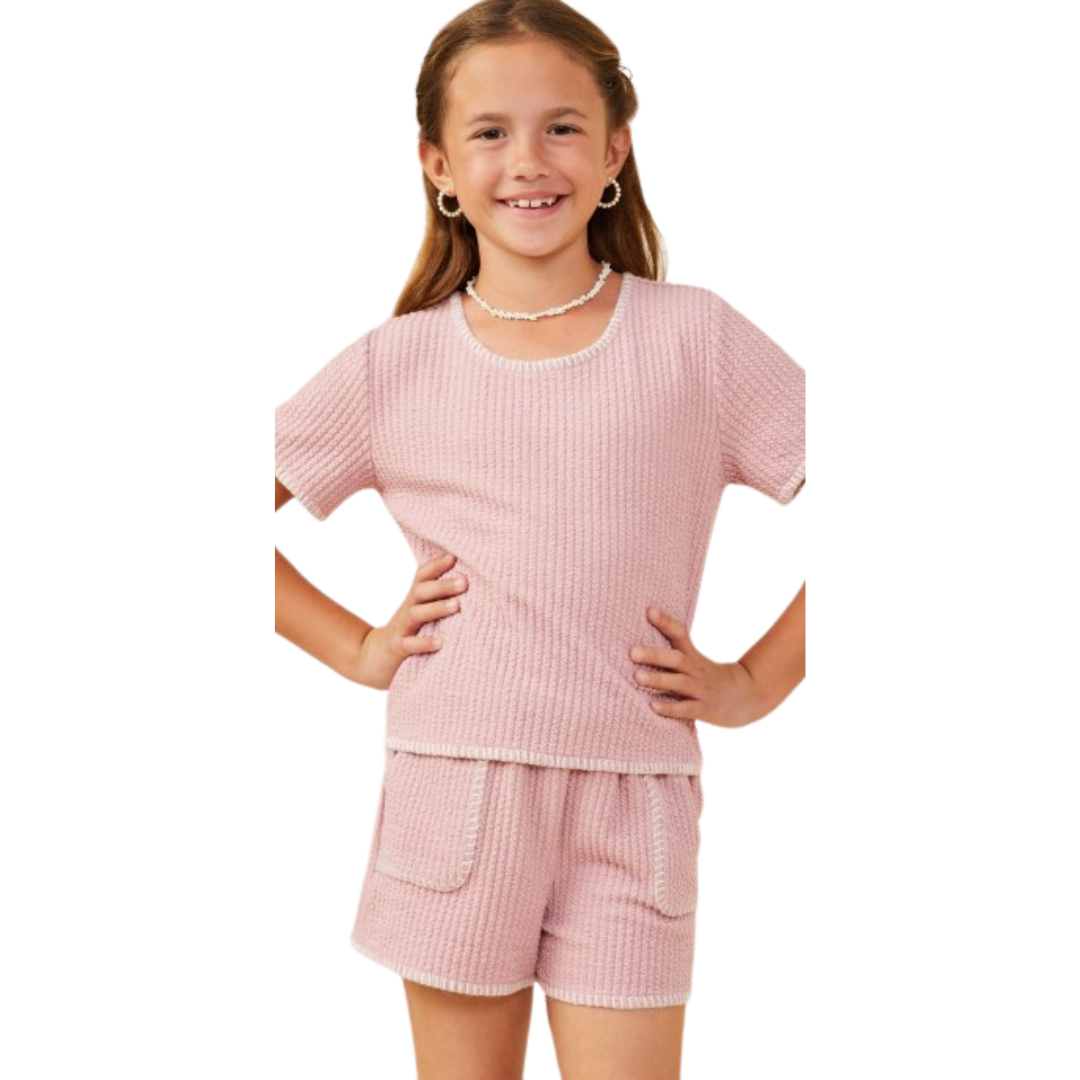 Girl smiling in a pink rib knit short-sleeve top and matching shorts with contrast white trim and front patch pockets.