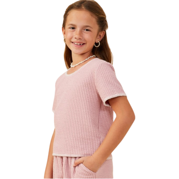 Side view of girl wearing textured pink lounge set with hands in pockets and white contrast trim details on sleeves and hem.