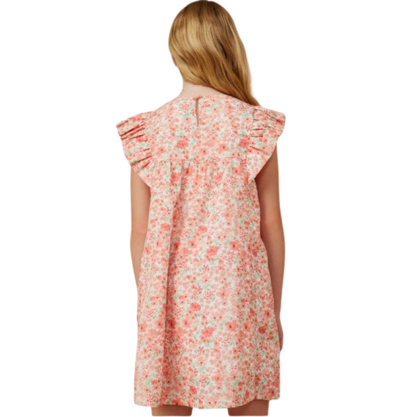 Girl wearing coral ditsy floral dress with ruffle sleeves and back keyhole button closure, hair down.
