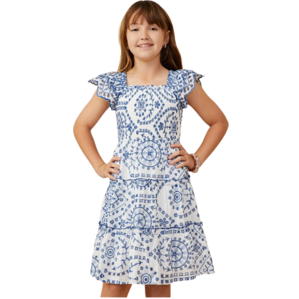 Girl wearing a white dress with blue embroidered patterns, scalloped flutter sleeves, and a square neckline.