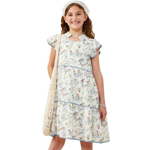 Girl facing forward wearing white floral dress with blue ribbon print and flutter sleeves