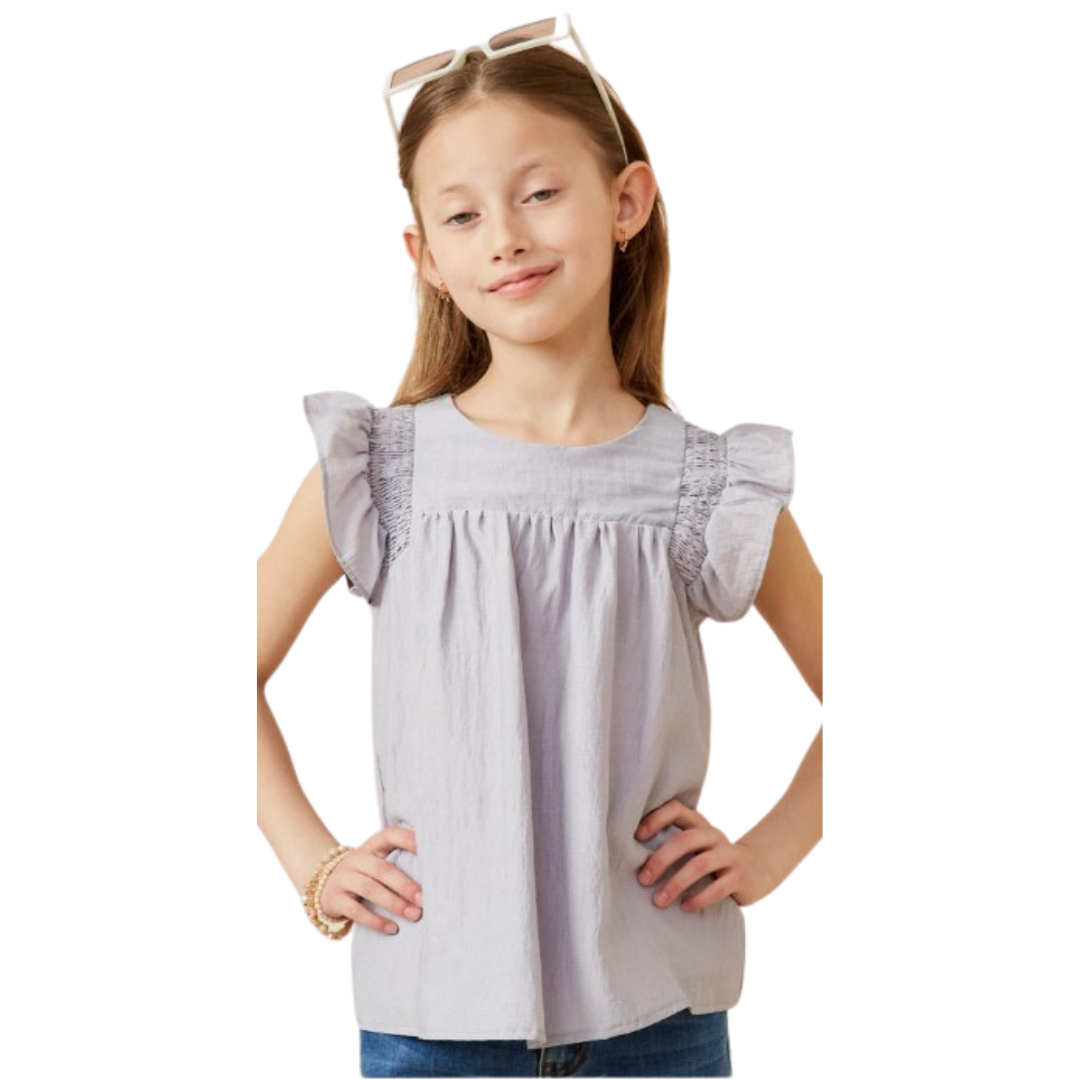 Girl wearing a lavender top with flutter sleeves, smocked shoulder details, and a flowy gathered front.