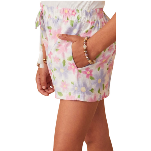 Close-up of pastel floral shorts with tassel-tie waist and hand in side pocket.
