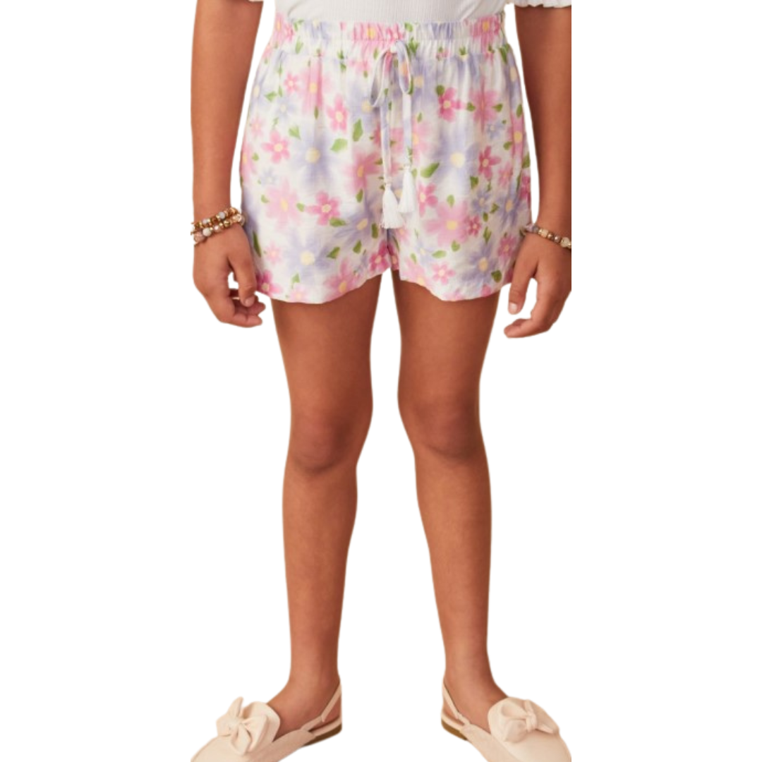 Girl wearing pastel floral pull-on shorts with tassel drawstring and pockets, paired with neutral slip-on shoes