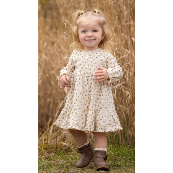 Toddler girl smiling outdoors in a floral tiered dress with long sleeves and brown boots.