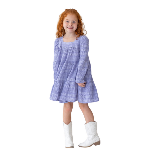 Young girl wearing the blue smocked dress with white cowboy boots, smiling and posing.