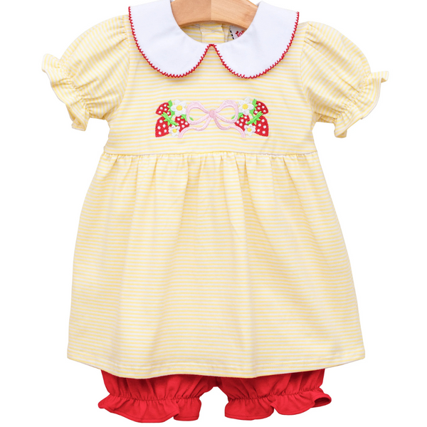 yellow top with a white rounded collar with red trim and strawberries, daisies, and a bow on the front. has matching red ruffle bloomers. 