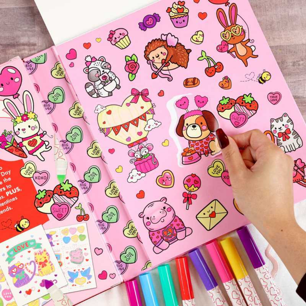 Colorful sticker book with cartoon characters and a hand holding markers on a wooden surface.