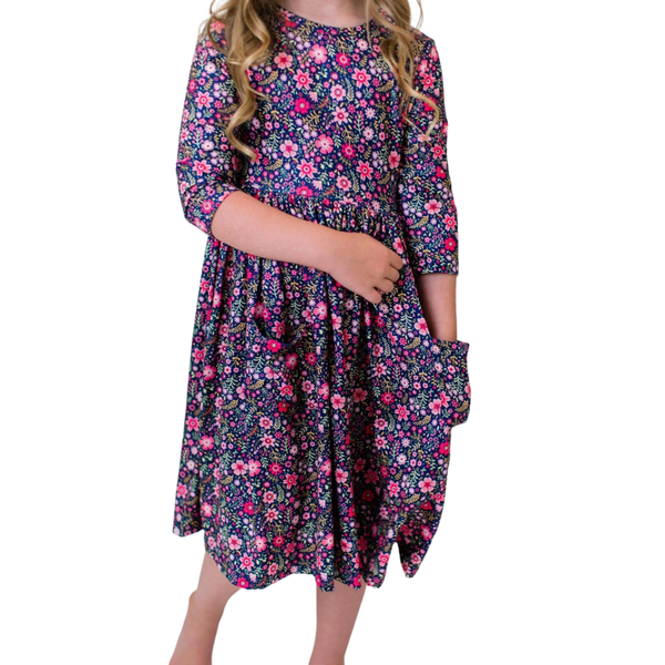 Girl wearing a navy floral long sleeve twirl dress with colorful pink flowers and convenient side pockets.